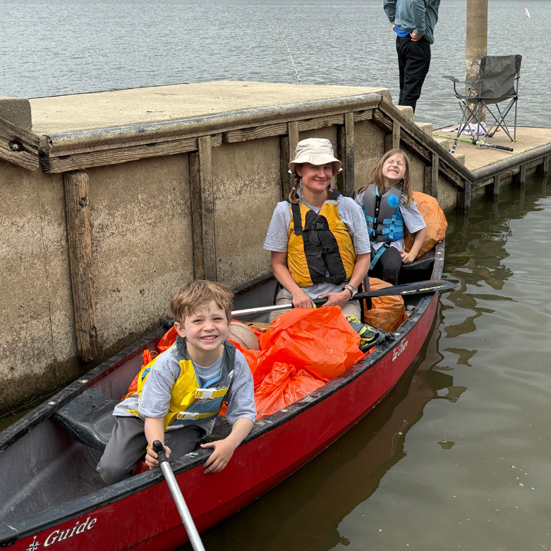A woman and two young children in a canoe with trash bags and trash grabbers